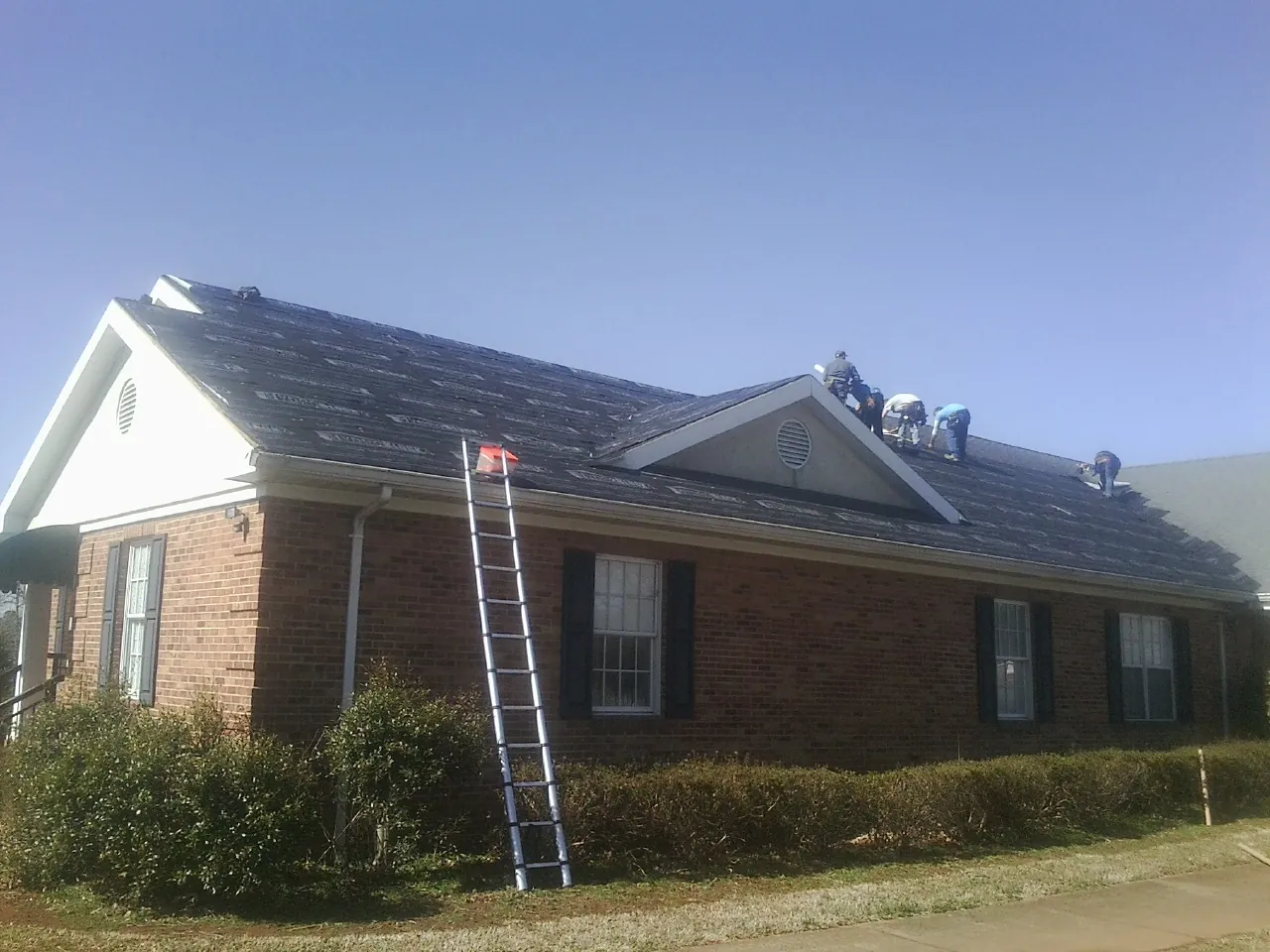 Crew tearing shingles off a brick ranch roof with a ladder set — Emergency Roof Repair work by our crew in Mount Angel