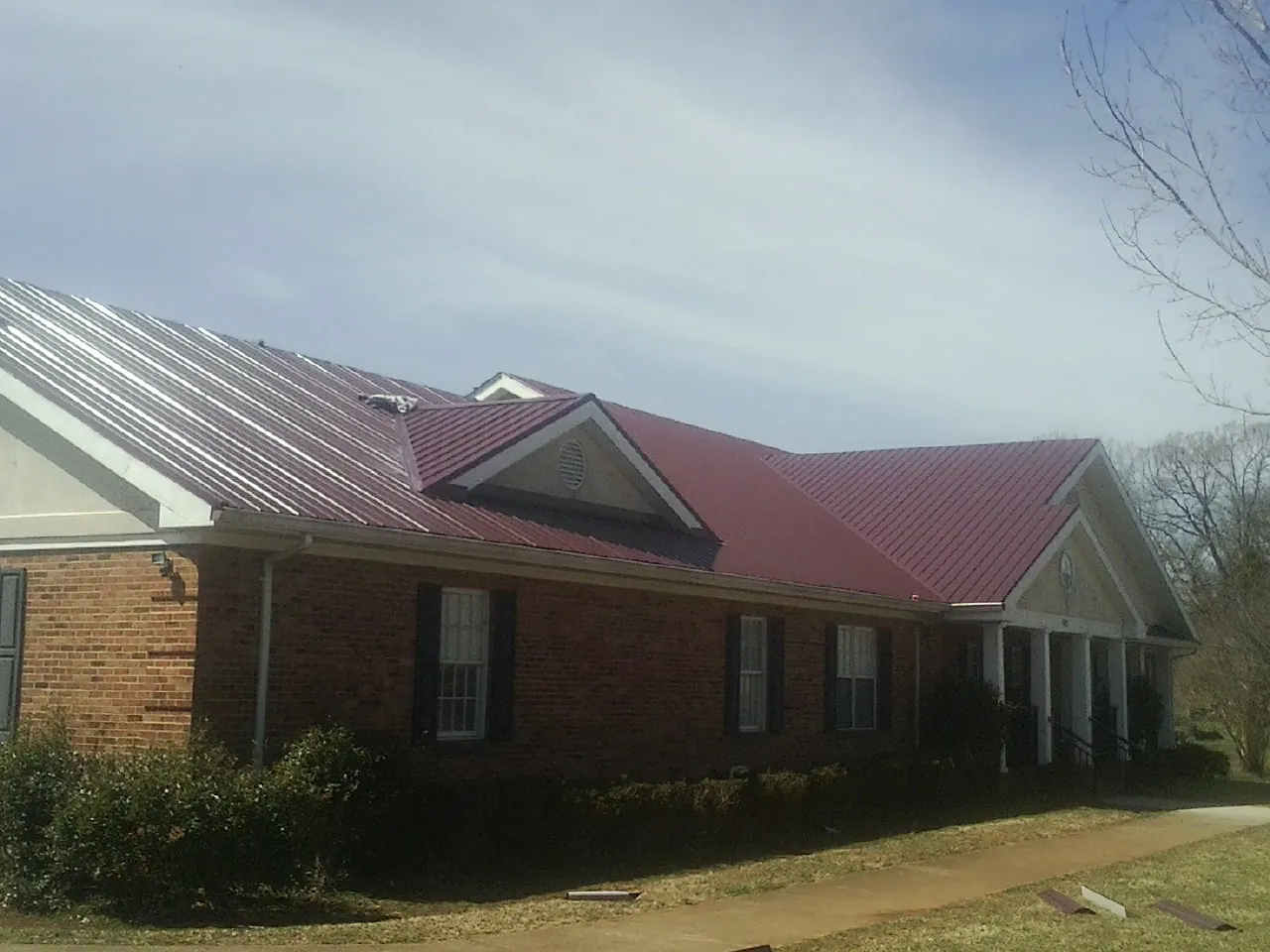 Red metal roof with gabled entries on a long brick building, from a Hail Damage Roof Repair job in Mount Angel