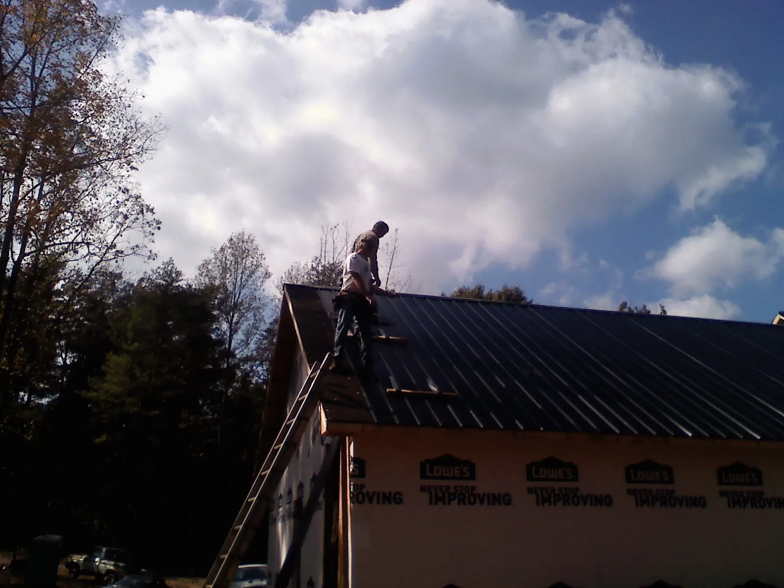 Roofer fastening dark metal panels high against a cloudy sky, from a Roof Inspection job in Mount Angel