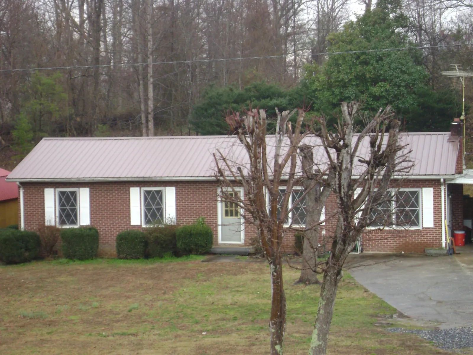 Mauve metal roof on a brick ranch home behind bare trees in Mount Angel
