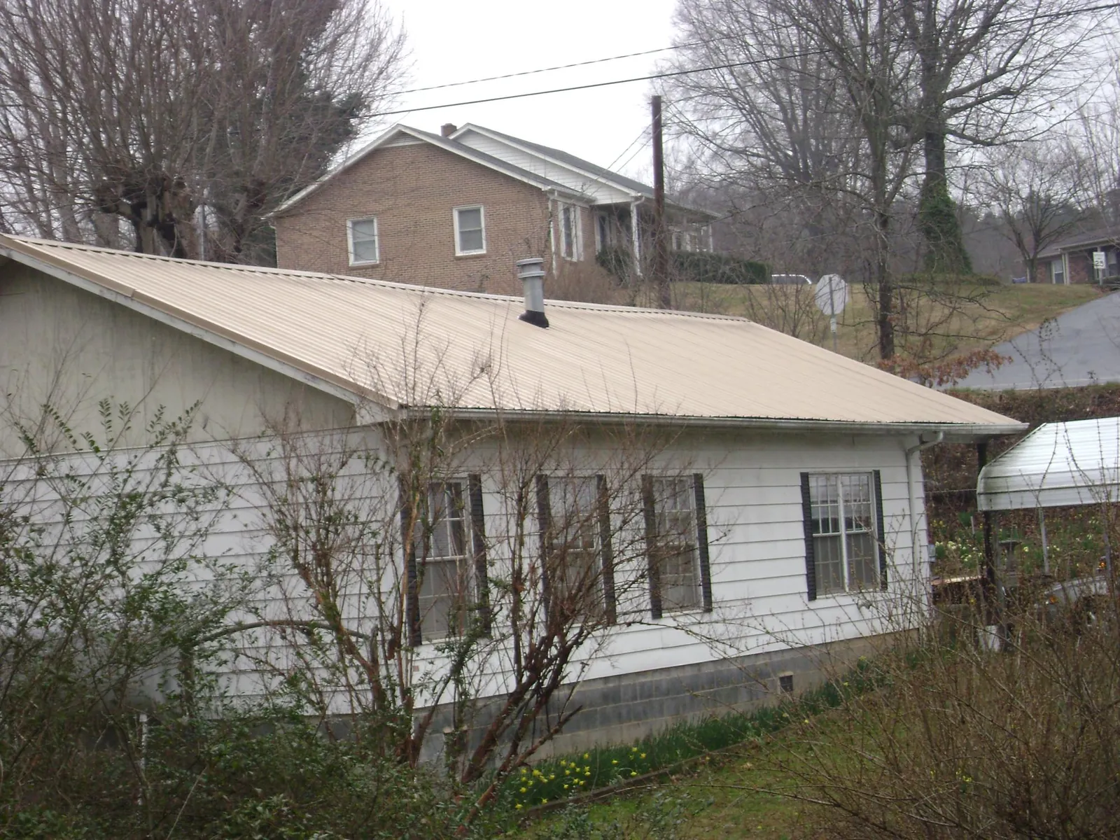 Tan metal roof on a white sided house set into a hillside — Commercial Roofing by Roofing Brothers in Mount Angel